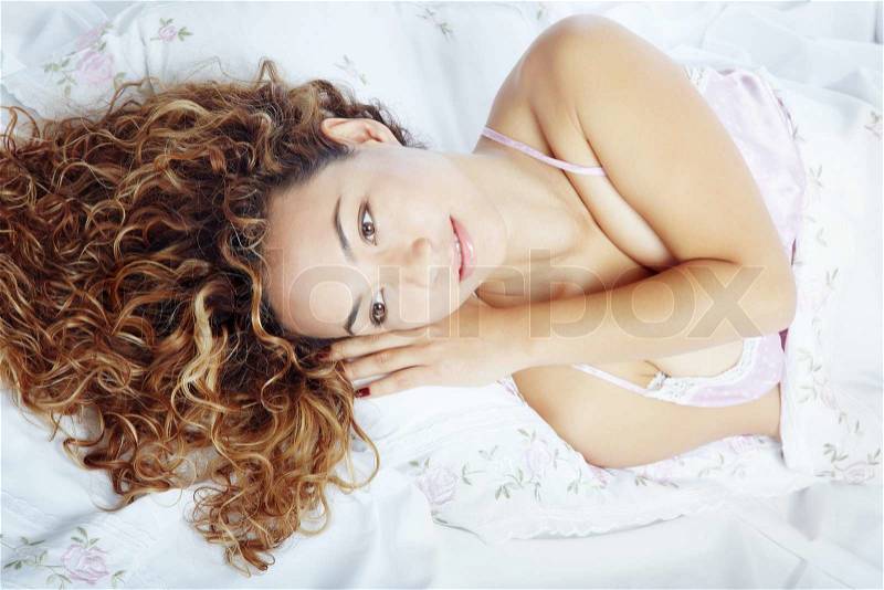 Pretty lady with curly hairs laying on a bed, stock photo