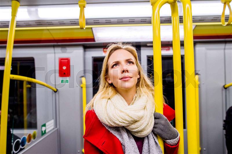 Beautiful young blond woman in red coat in subway train, stock photo