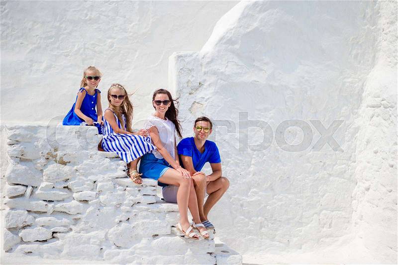Family vacayion in Europe. Parents and kids at street of typical greek traditional village with white walls and colorful doors on Mykonos Island, in Greece, stock photo