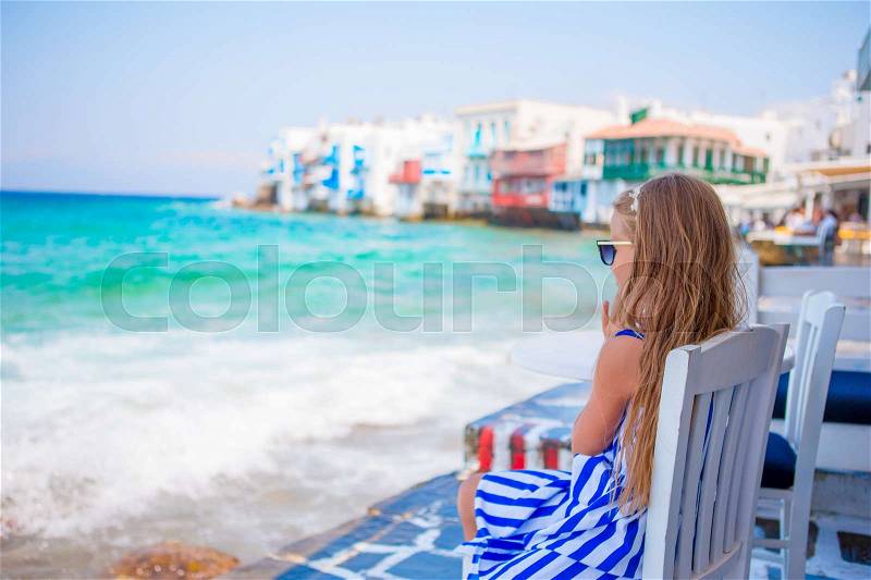 Adorable little girl at Little Venice the most popular tourist area on Mykonos island, Greece. Beautiful kid smile and look in the camera on Little Venice background, stock photo
