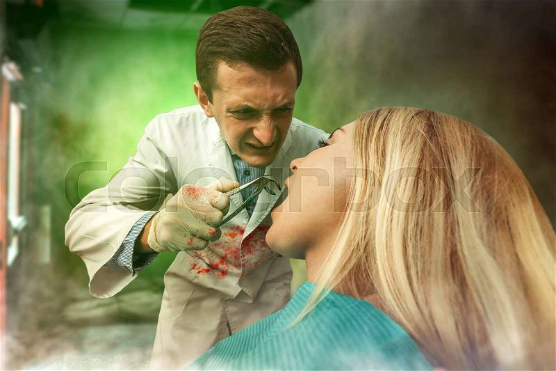Mad bloodstained dentist extracting a tooth in woman, strange smoke is in the air, stock photo