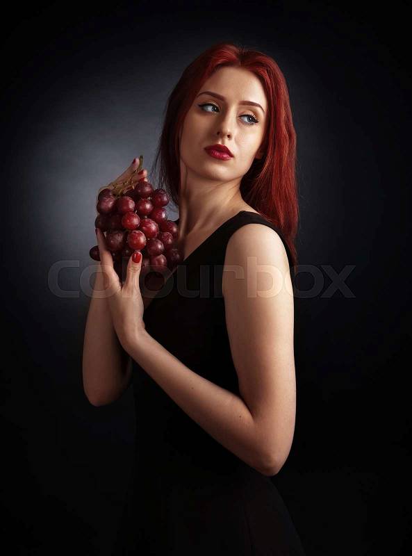 Beautiful redheaded woman in a black dress with grape, stock photo
