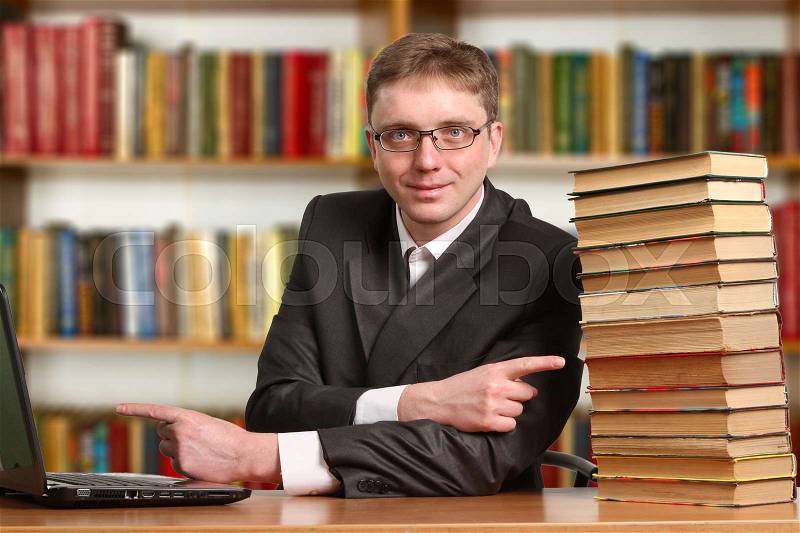 Portrait of clever student with open book reading it in college library, stock photo