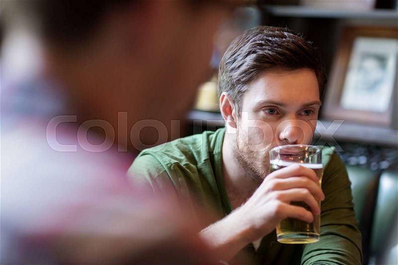 People, leisure, friendship and communication concept - happy man with friend drinking beer at bar or pub, stock photo