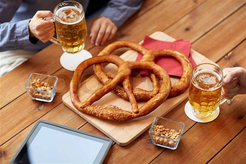 People, leisure, technology and drinks concept - close up of male friends drinking beer with pretzels, peanuts and tablet pc computer on table at bar or pub, stock photo