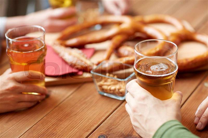 People, leisure and drinks concept - close up of male hands with beer glasses, pretzels and peanuts at bar or pub, stock photo