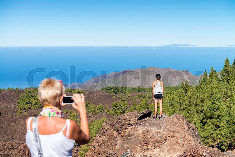 Back view of mother taking a picture of daughter on a mountain scenario, stock photo