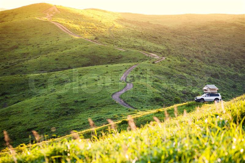 Car with rooftop tent in green hills, stock photo