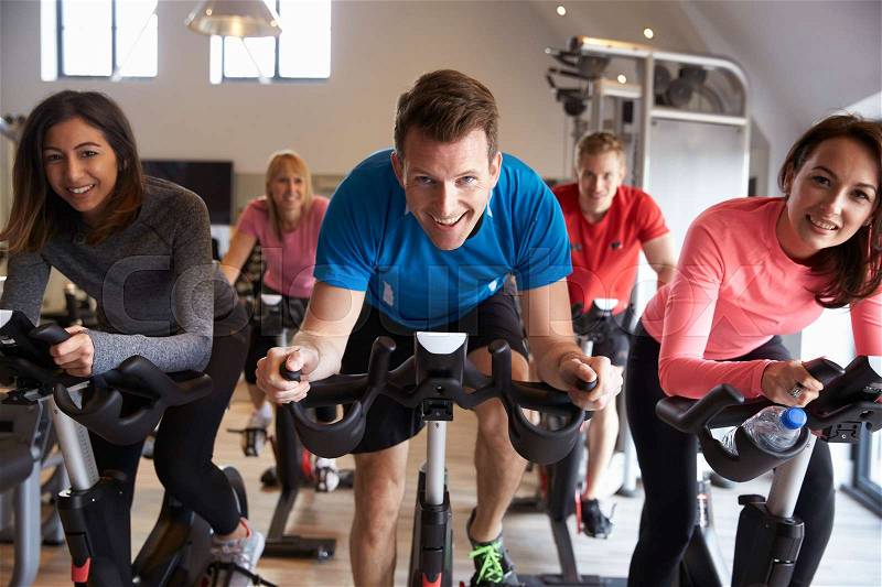 Spinning class on exercise bikes at a gym looking to camera, stock photo