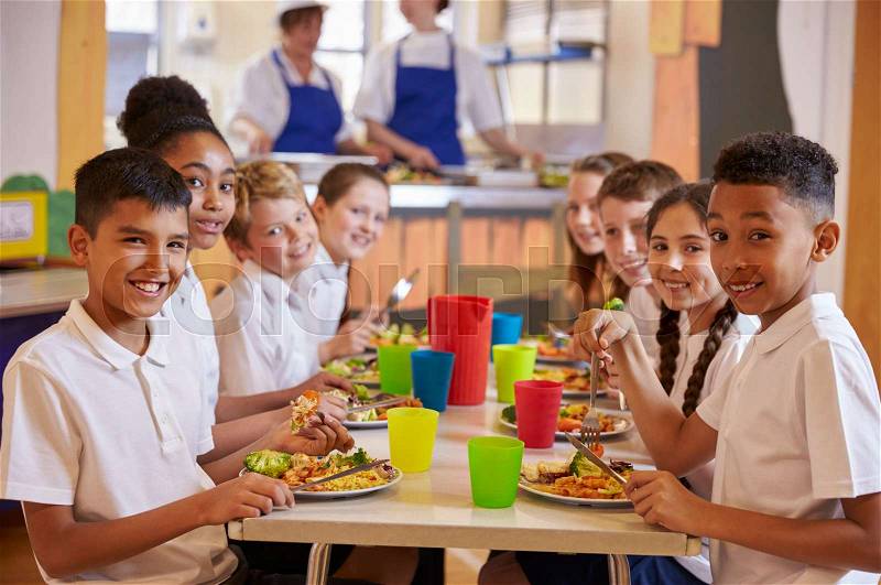 Kids at a table in a primary school cafeteria look to camera, stock photo