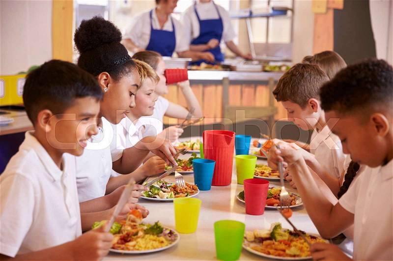Primary school kids eating at a table in school cafeteria, stock photo