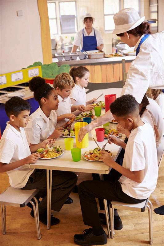 Primary school kids eat lunch in school cafeteria, vertical, stock photo