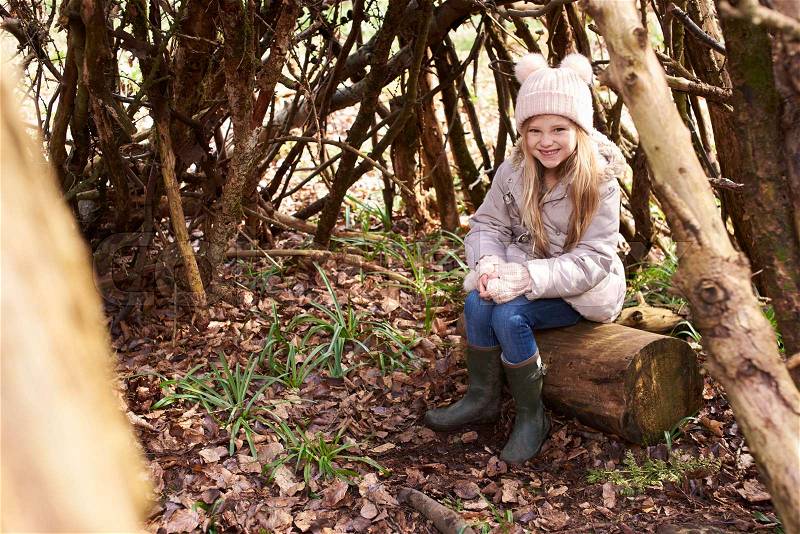 Young girl sitting in a forest shelter made of tree branches, stock photo