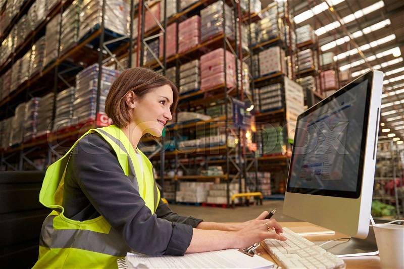 Woman working at computer in on-site office of a warehouse, stock photo