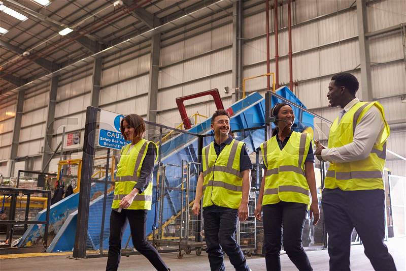 Four coworkers talk as they walk in an industrial interior, stock photo
