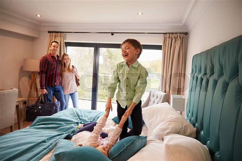 Family On Vacation With Children Playing On Hotel Bed, stock photo