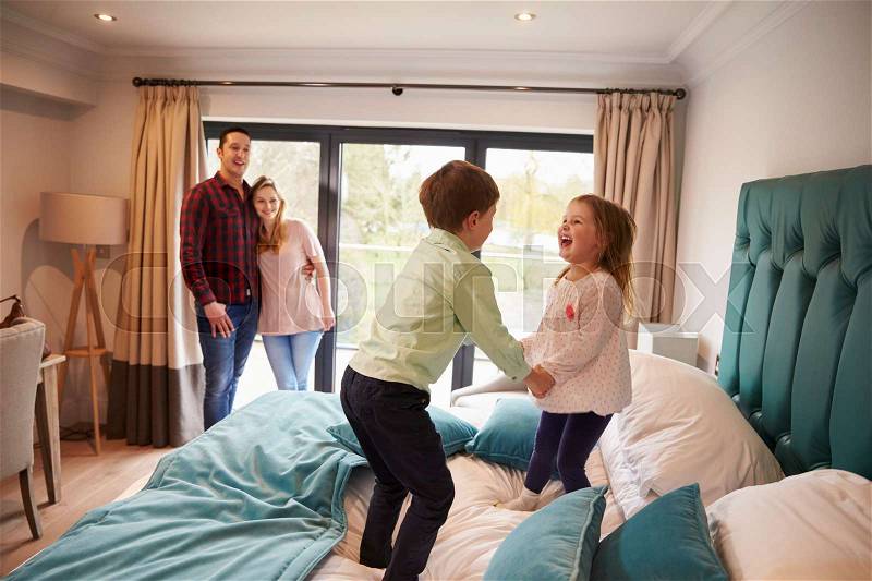 Family On Vacation With Children Playing On Hotel Bed, stock photo