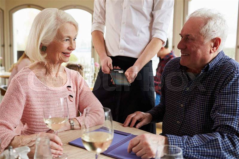 Senior Couple With Waiter Paying Bill In Restaurant, stock photo