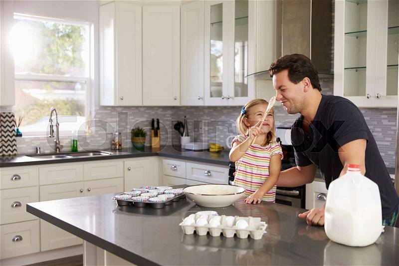 Girl putting cake mix on dad’s nose while they bake together, stock photo