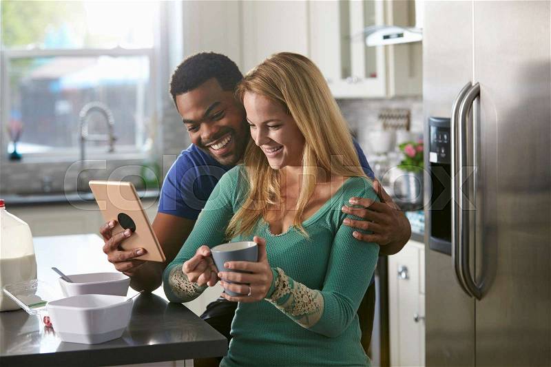 Mixed race couple looking at a tablet computer together in kitchen, stock photo