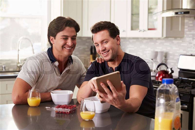 Male gay couple looking at tablet computer over breakfast, stock photo