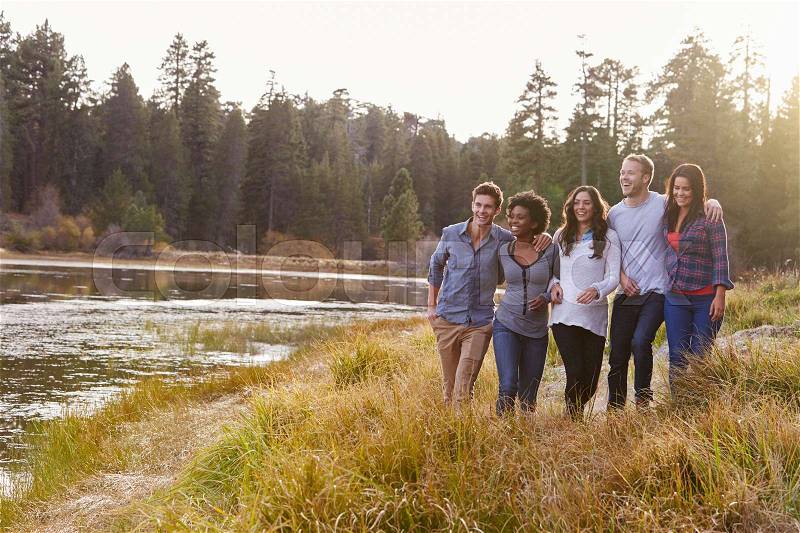 Group of five happy friends walking near a rural lake, stock photo