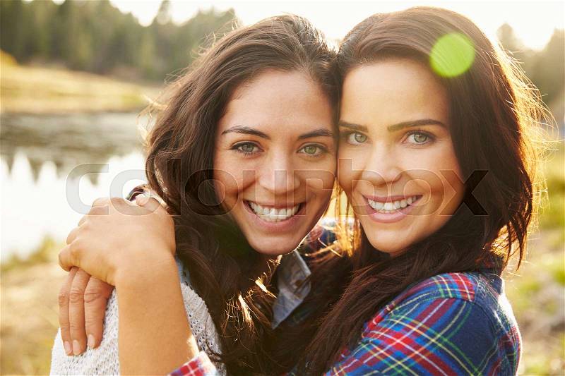 Lesbian couple hugging by a lake look to camera, close up, stock photo