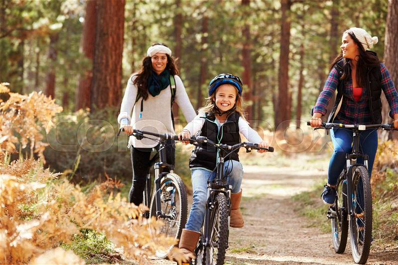 Lesbian couple cycling in a forest with their daughter, stock photo
