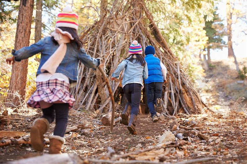 Three kids play outside shelter made of branches in a forest, stock photo