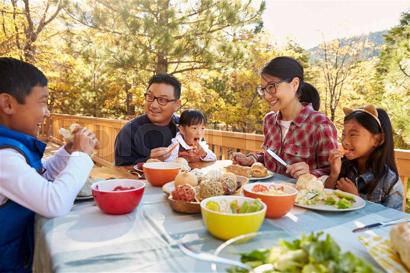 Asian family eating outside at a table on a deck in a forest, stock photo
