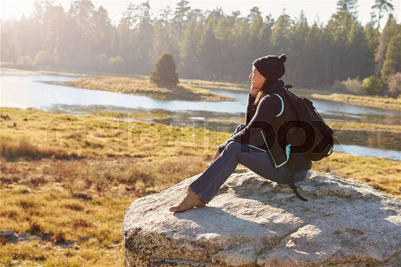 Young woman sits on a rock in countryside admiring the view, stock photo