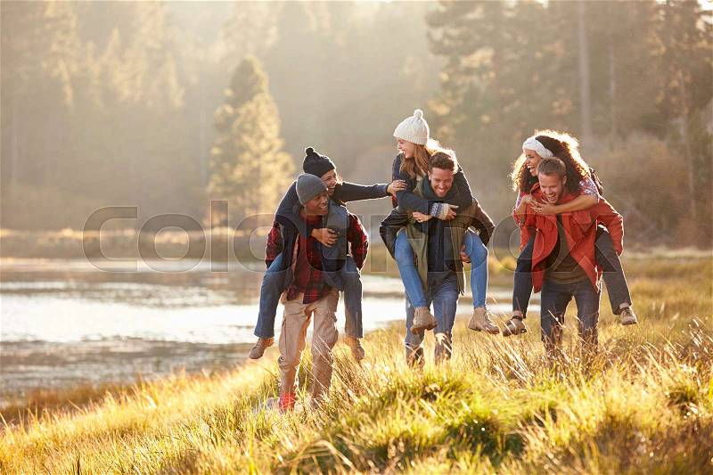Six friends have fun piggybacking in the countryside by lake, stock photo
