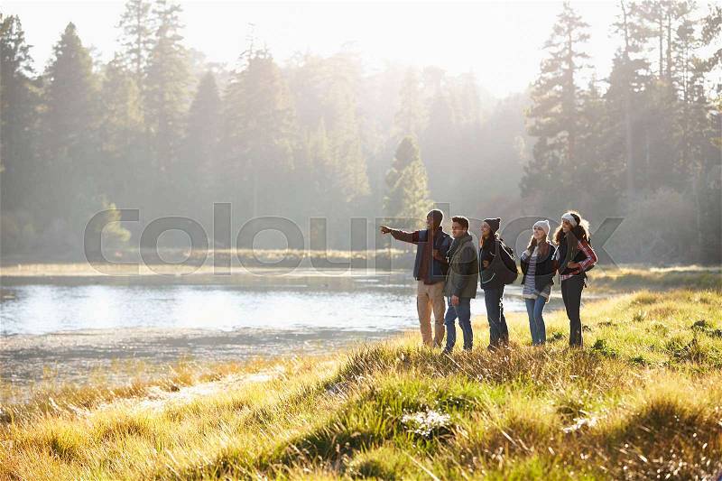 Five friends walking near a lake take in view, one points, stock photo