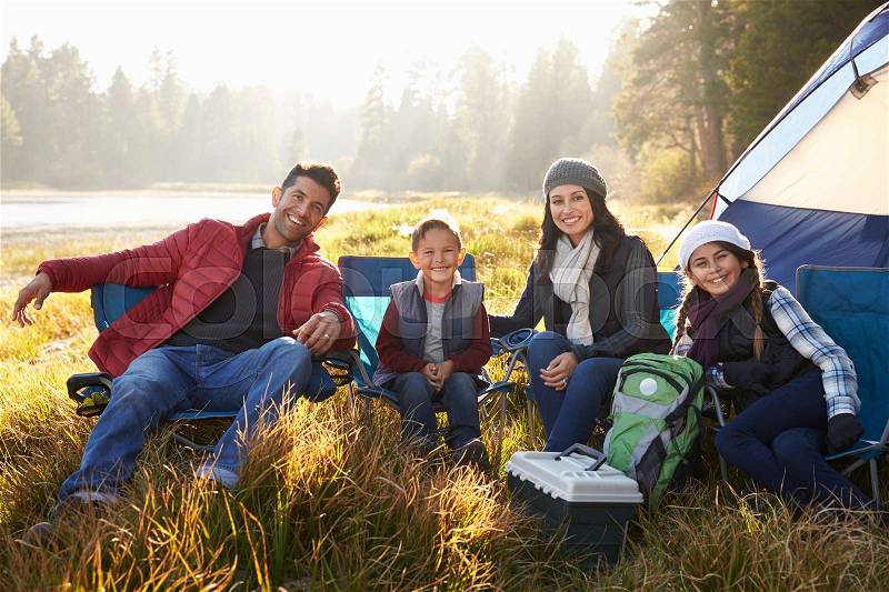 Happy family on a camping trip sit by tent looking to camera, stock photo