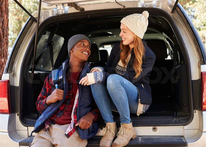 Mixed race couple in open back of car looking at each other, stock photo