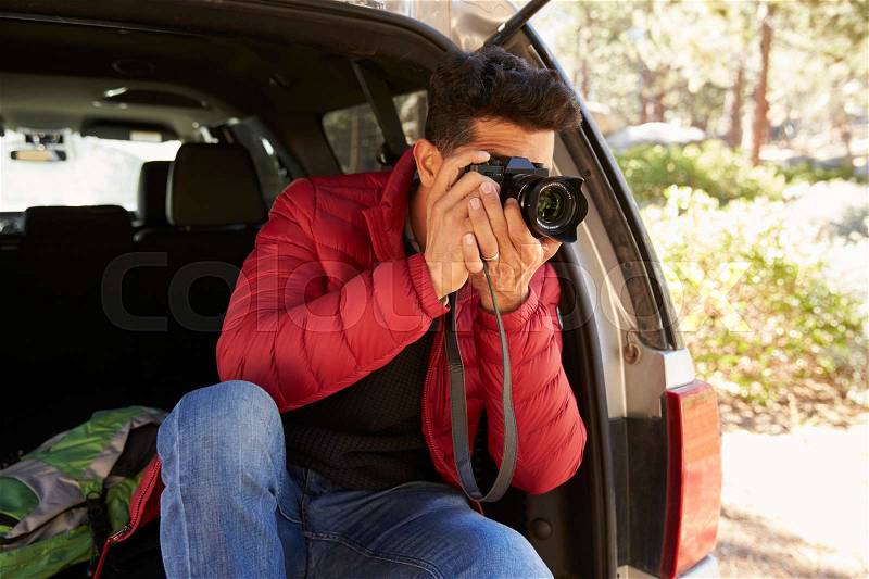 Man sitting in the open back of car taking photos, close up, stock photo