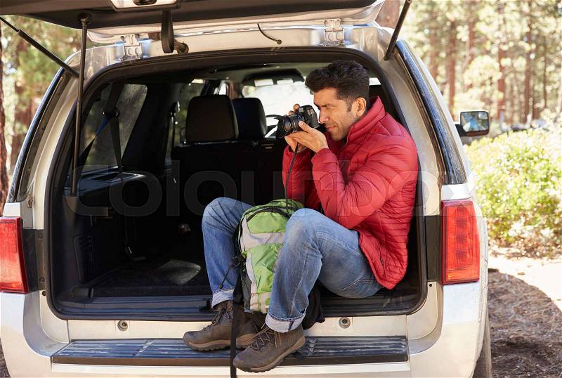 Man sitting in the open back of car taking photos in forest, stock photo