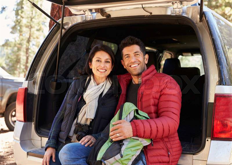 Happy Hispanic couple sitting in open back of car before hike, stock photo