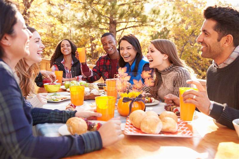 Group of happy friends eat and laugh at a table at a barbecue, stock photo