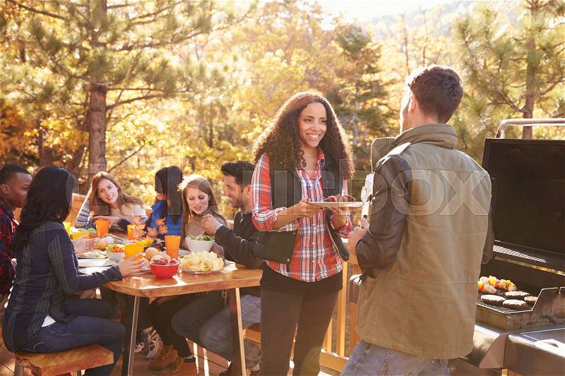 Friends eat at table and two talk by the grill at a barbecue, stock photo