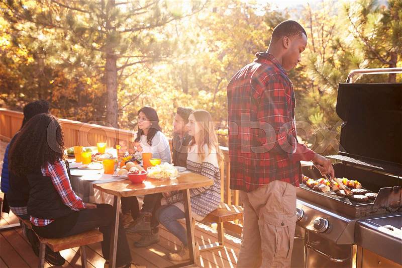 Man barbecues for friends at a table on a deck in a forest, stock photo