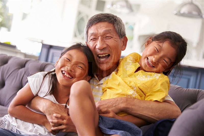 Grandfather And Granddaughters Relaxing On Sofa At Home, stock photo