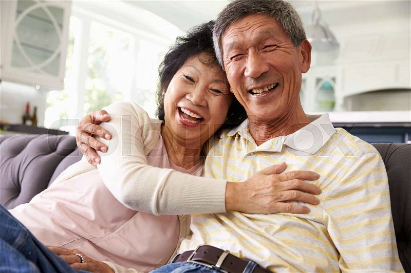 Senior Asian Couple At Home Relaxing On Sofa Together, stock photo