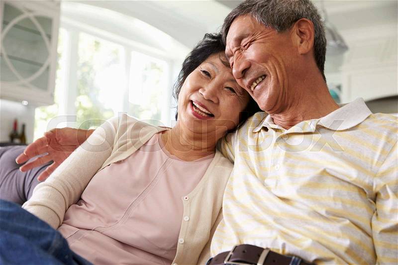 Senior Asian Couple At Home Relaxing On Sofa Together, stock photo