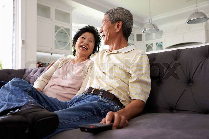 Senior Asian Couple At Home On Sofa Watching TV Together, stock photo