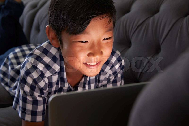 Boy Relaxing On Sofa At Home Using Laptop, stock photo