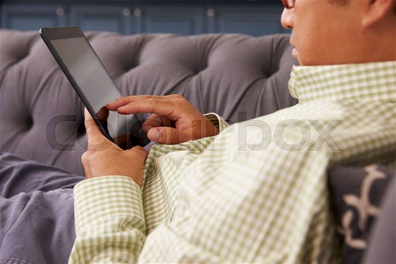 Man Relaxing On Sofa At Home Using Digital Tablet, stock photo