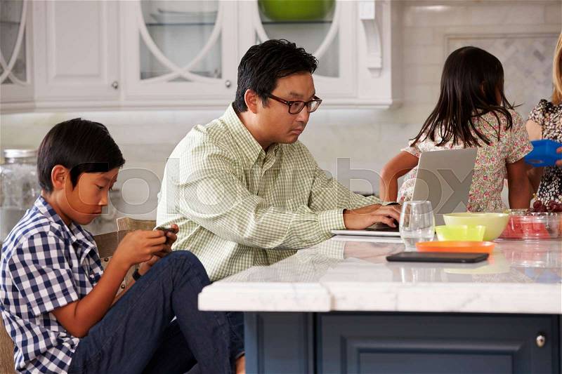 Family In Kitchen Having Breakfast And Using Digital Devices, stock photo