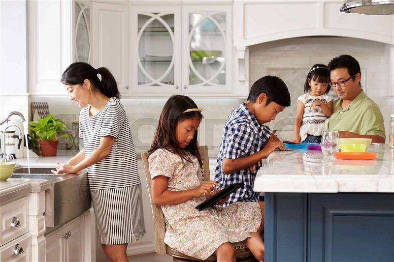 Family In Kitchen Doing Chores And Using Digital Devices, stock photo
