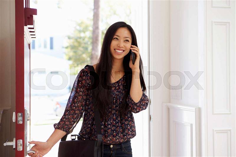Woman Opening Front Door Whilst Talking On Mobile Phone, stock photo